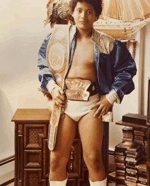 a young man wearing a wrestling belt stands in front of a stack of cd 's