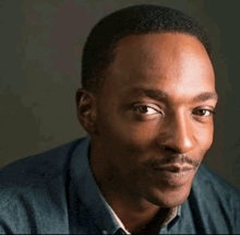a close up of a man 's face with a mustache and a blue shirt .