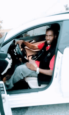 a man in a red shirt and black vest is sitting in the driver 's seat of a white car