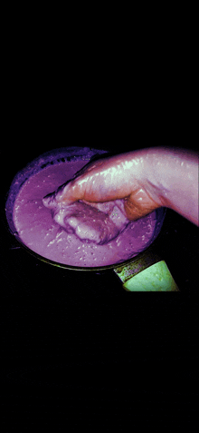 a person 's hand is reaching into a pot of purple liquid