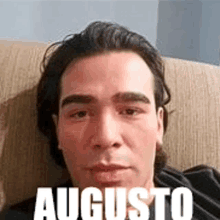 a man is laying on a couch with the name augusto written on his face .