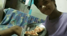 a young boy in a purple shirt holds a plate of pizza