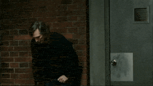 a man in a black sweater is standing in front of a red brick wall
