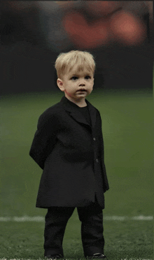 a little boy wearing a black suit is standing on a field