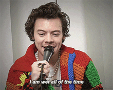 a man wearing a colorful sweater is holding a microphone and says i am wet all of the time