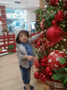 a child stands in front of a christmas tree with a sign that says rihappy