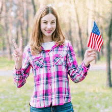 a woman is holding an american flag and giving a peace sign .