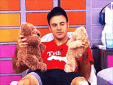 a man in a red shirt is holding two teddy bears in his lap .