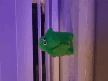 a green stuffed animal with big eyes is sitting on a window sill