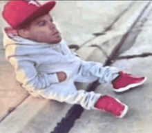a little boy wearing a red hat and red shoes is sitting on a curb