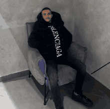 a man is sitting in a chair wearing a black balenciaga jacket