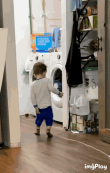 a little boy standing in front of a washer and dryer with a box of tide pods on the wall