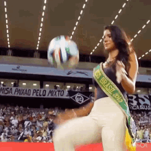 a woman in a miss brasil 2013 sash kicking a soccer ball