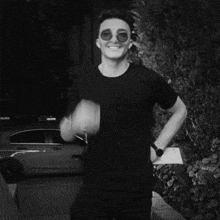 a man wearing sunglasses and a black shirt is smiling in front of a car