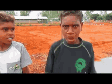 two young boys are standing next to each other in a dirt field and one of them is wearing a shirt that says enjoy