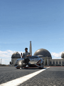 a man is sitting in front of a sports car looking at his phone