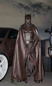 a person in a batman costume is standing in front of a car .