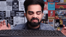 a man with a beard is holding a keyboard in front of a wall with posters including one that says do more