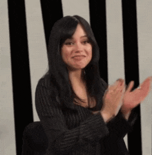 a woman in a striped shirt is clapping her hands in front of a black and white striped wall .