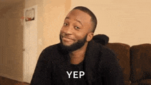 a man with a beard is sitting on a couch in a living room with a basketball hoop in the background .