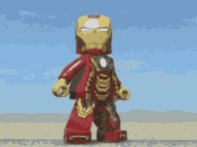 a lego figure of iron man is standing on a sandy surface .