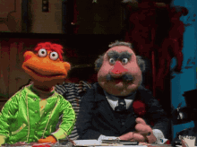 two muppets are sitting at a table and one of them has a pink nose