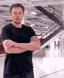 elon musk is standing in a room with his arms crossed and looking at the camera .