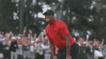 a man in a red shirt and black pants is standing on a golf course in front of a crowd .