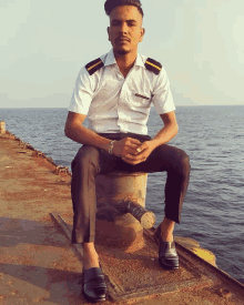 a man in a white shirt and black pants sits on a rusty pillar