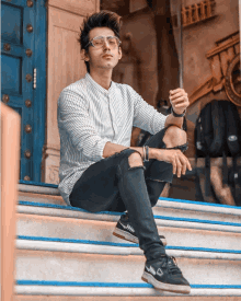 a young man sitting on a set of stairs wearing glasses