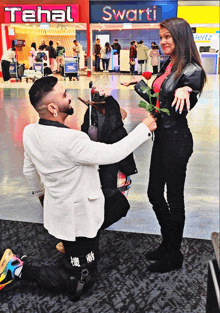 a man kneeling down in front of a woman holding a rose in front of a tehal sign