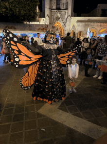 a woman dressed as a skeleton with butterfly wings stands in front of a crowd