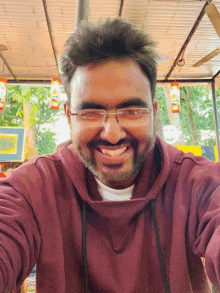 a man wearing glasses and a maroon hoodie smiles