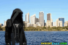 a man in a hooded jacket is standing in front of a city skyline and a body of water