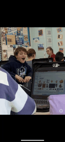 a boy wearing a sweatshirt that says ' ucsd ' on it sits in front of a laptop