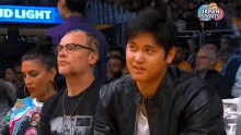 a man in a black leather jacket is sitting in the stands at a basketball game with a bud light sign in the background