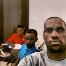 a man taking a selfie with two young boys in the background