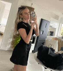 a woman in a black dress is taking a selfie in front of a black fridge