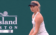 a woman in a white tank top is serving a tennis ball in front of a scoreboard that says stellar