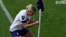 a woman in a white shirt and blue shorts is standing next to a flag on a soccer field ..