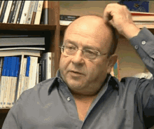 a man with glasses scratches his head in front of a bookshelf with a book titled " a dictionary " on it