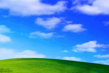 a green hill with a blue sky and white clouds behind it