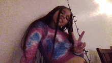 a girl in a tie dye shirt is giving the peace sign