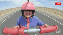 a little girl wearing a pink helmet and a blue jacket is riding a red pipe on a road with a live sign above