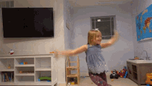 a little girl is dancing in a living room with a map of the world on the wall behind her .