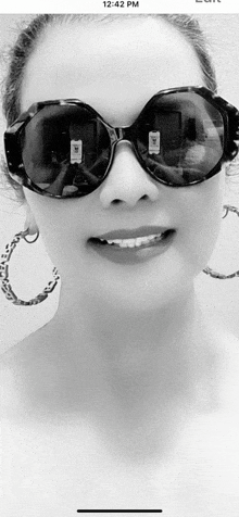 a woman wearing sunglasses and hoop earrings is smiling in a black and white photo