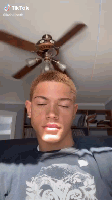 a young man is sitting in front of a ceiling fan in a living room with his eyes closed .