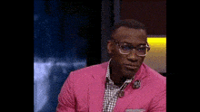 a man wearing a pink suit and glasses is smiling while sitting on a stage .