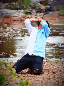 a man in a blue shirt is kneeling down in front of a body of water