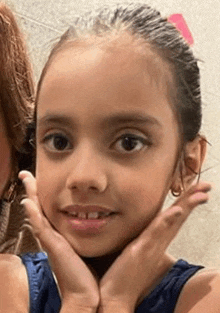 a little girl is holding her face with her hands and smiling for the camera .